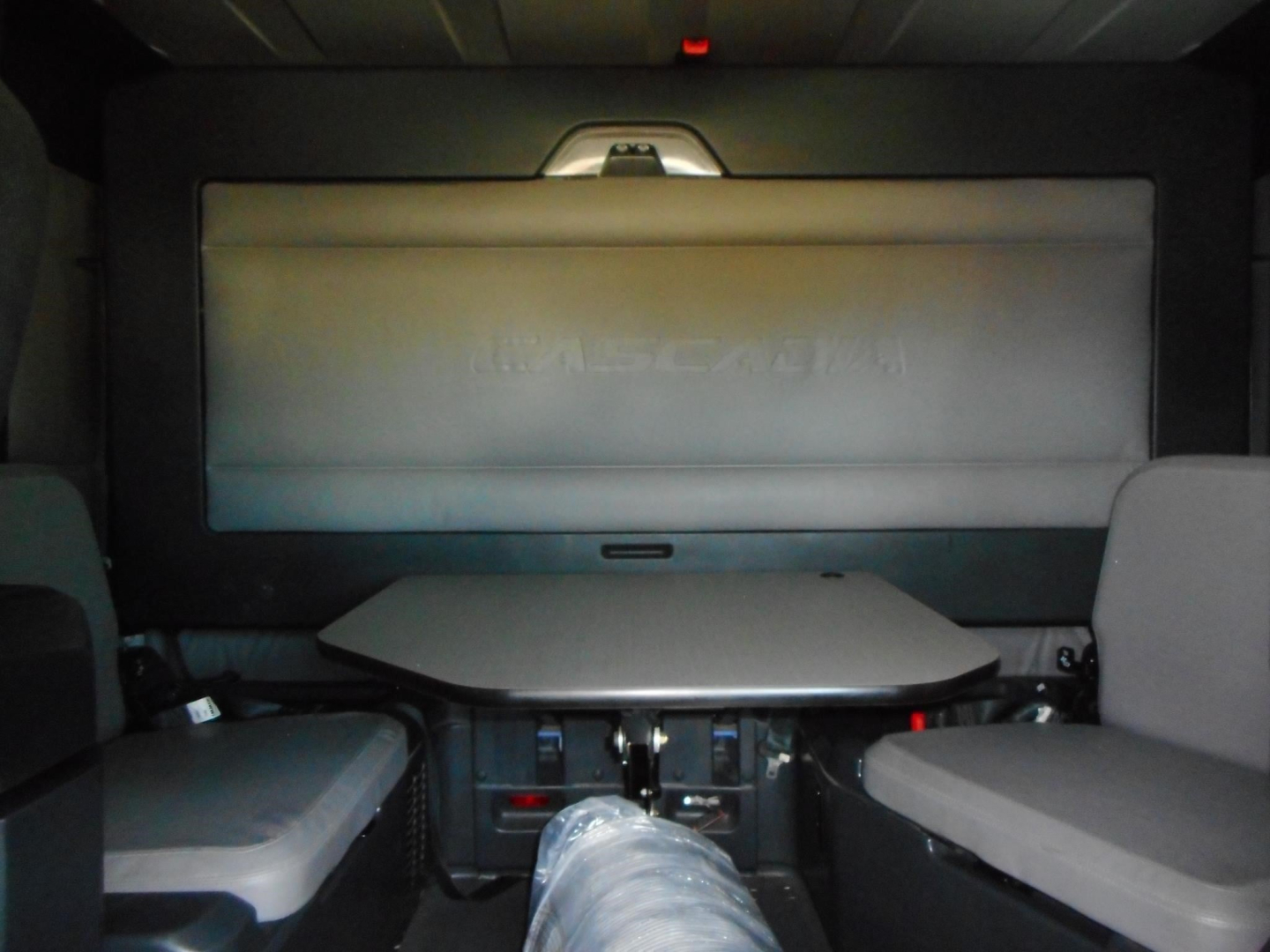 Cab interior of a Freightliner Cascadia sleeper showing a fold-down table and rear-wall screen with seating on both sides.
