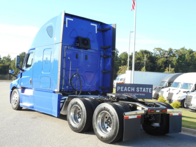 2022 Freightliner Cascadia 126 sleeper cab truck, blue exterior, rear view showing triple axles and fifth wheel mounting area, visible Peach State Trucks sign in background.