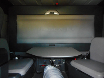 Cab interior of a Freightliner Cascadia sleeper showing a fold-down table and rear-wall screen with seating on both sides.