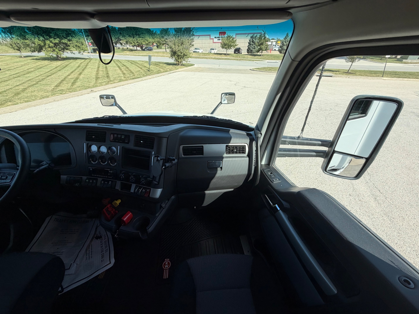 Kenworth T680 truck cabin interior view from the driver's seat showing dashboard controls, steering wheel, side mirror, and windshield.