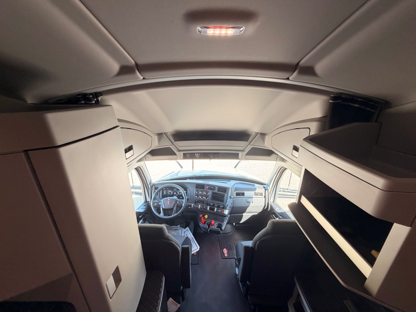 Kenworth T680 cab interior view showing dash, steering wheel, and upper bunk storage compartments.