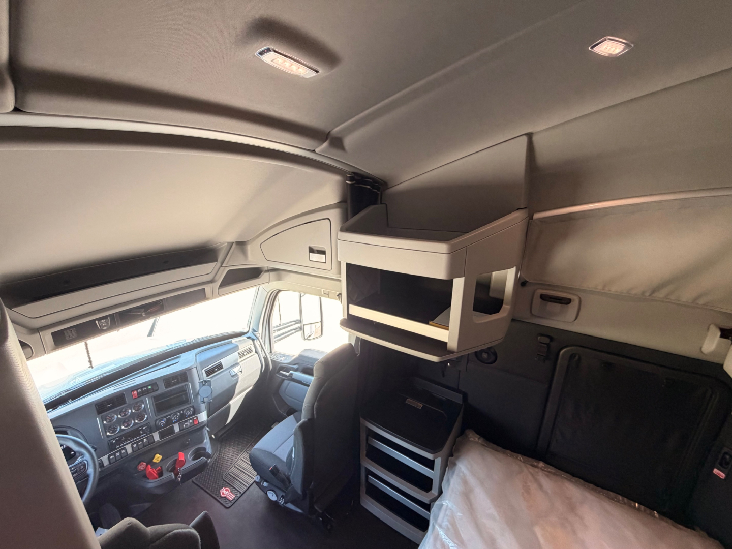 Kenworth T680 sleeper cab interior showing overhead storage shelf and cockpit with steering wheel and dash.