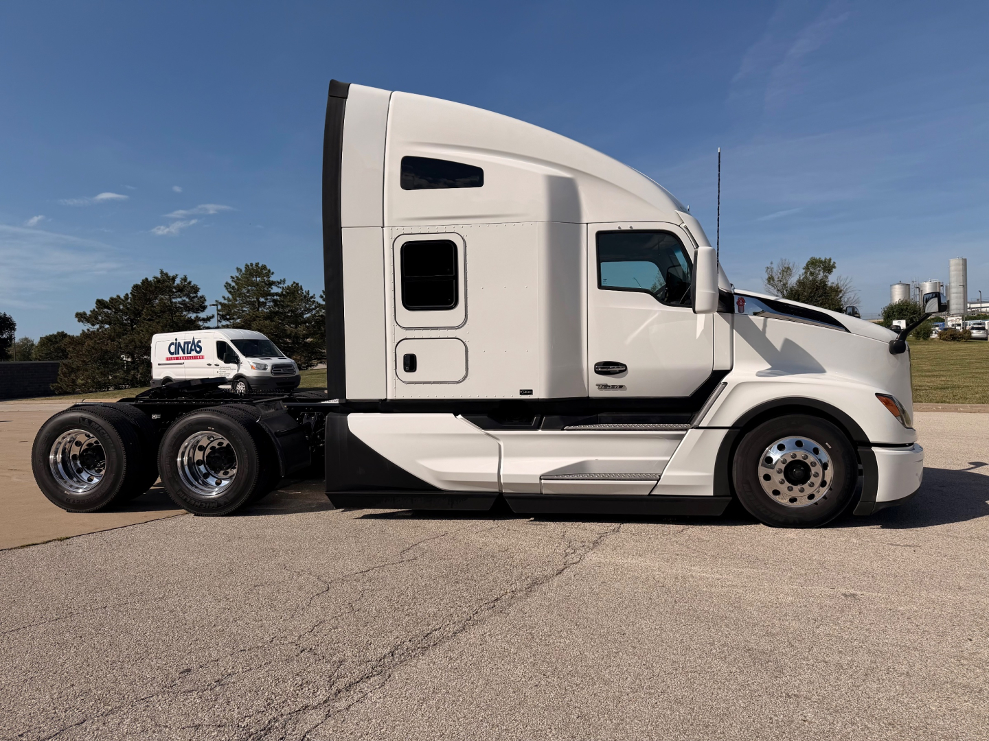 Kenworth T680 side view showing sleeper cab, white exterior, chrome wheels, and rear trailer hitch undercarriage.