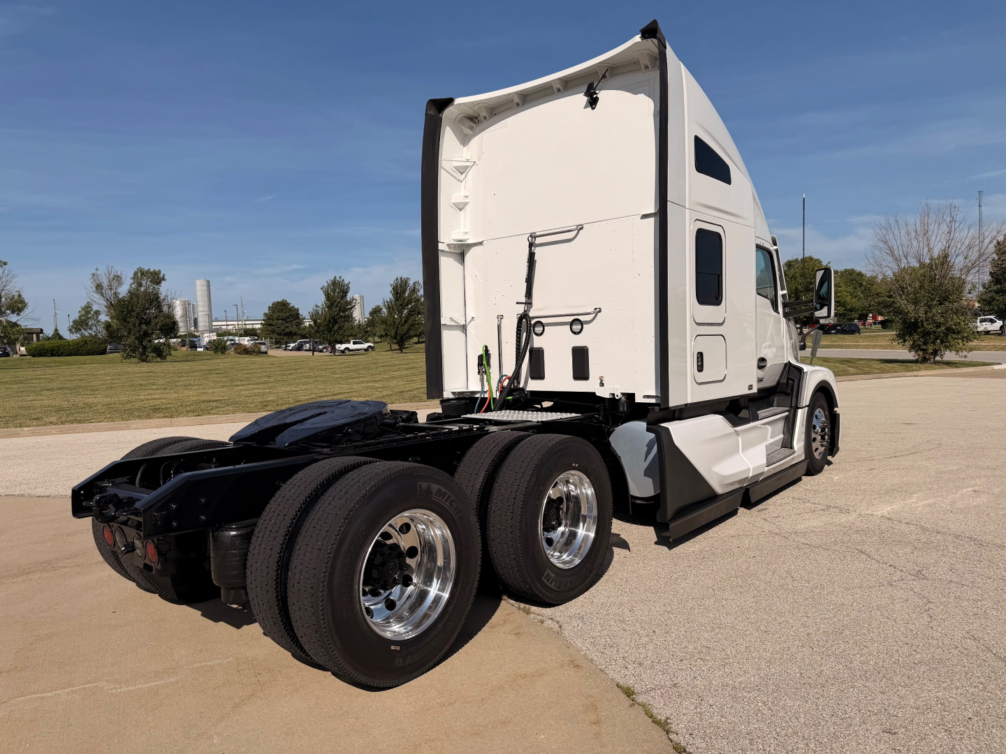 Kenworth T680 tractor truck cab with sleeper in white, rear triple-axle configuration, fuel and electrical lines visible near fifth wheel.