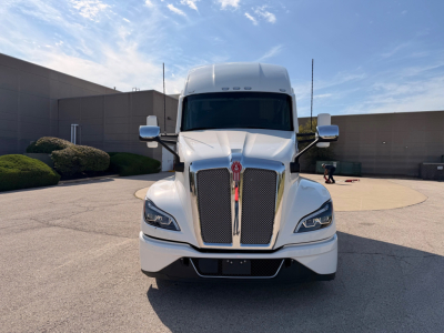 Kenworth T680 truck front view showing grille, headlights, and emblem; white exterior; tall sleeper cabin; side mirrors visible.