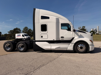 Kenworth T680 side view showing sleeper cab, white exterior, chrome wheels, and rear trailer hitch undercarriage.