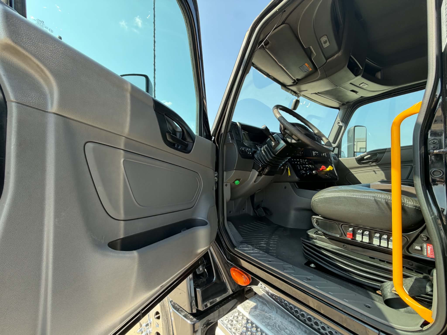 Truck interior view of the cab from the driver’s side door open, showcasing the steering wheel, dashboard controls, and driver seat in a 2023 International LT625 sleeper tractor.