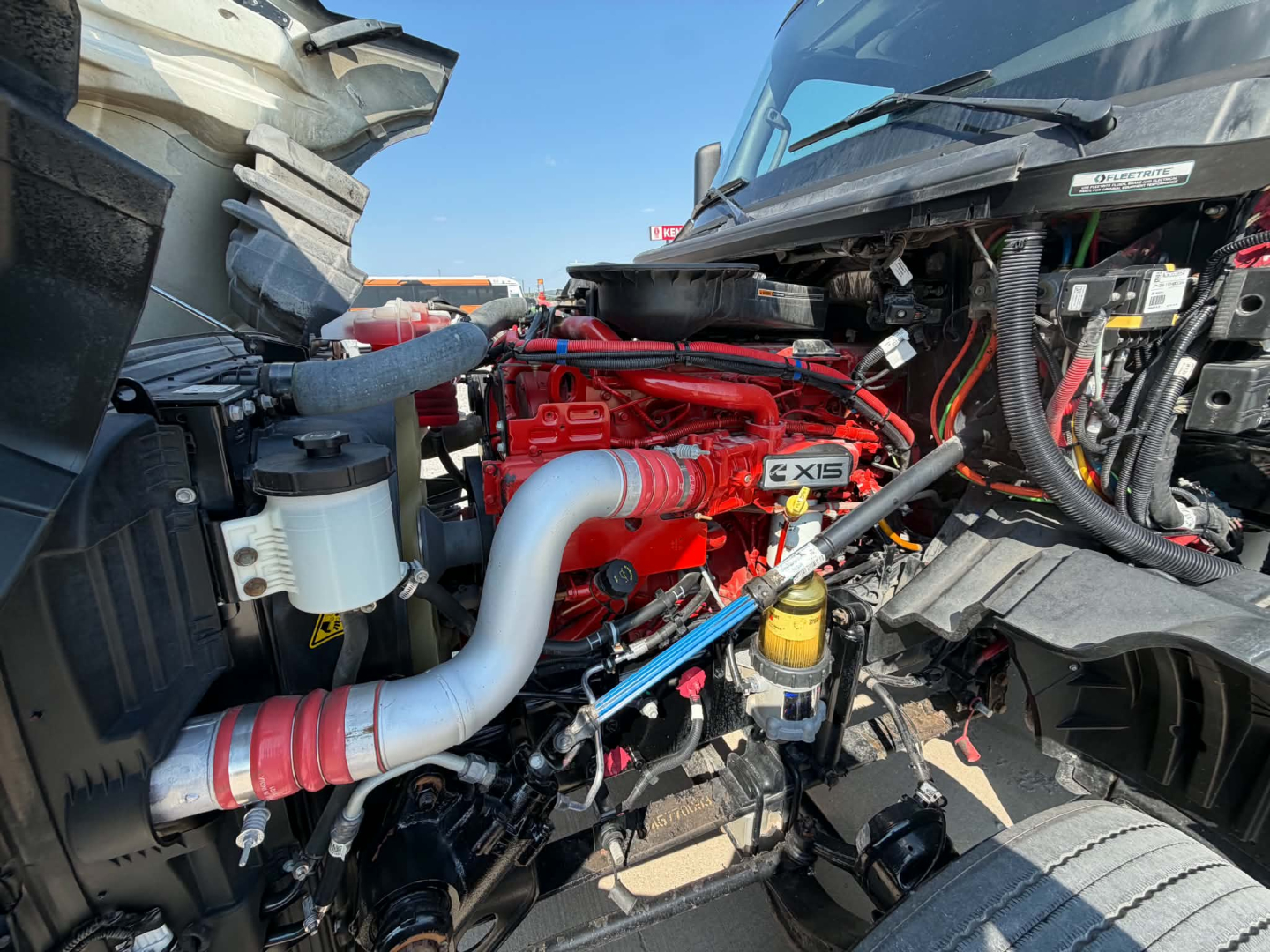 Truck engine bay of a 2023 International LT625 showing red engine block, large gray intercooler piping, coolant reservoir, and various hoses and cables.