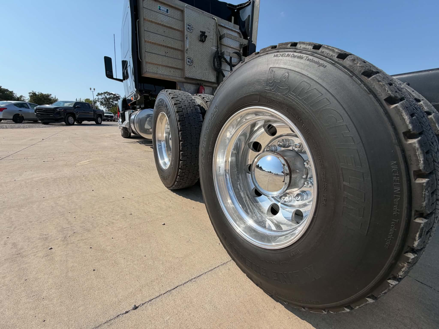 Truck front wheel and open sleeper cab showing chrome dual rear wheels and prominent Kumho tire; side of truck shows steps and storage area with metal panels.