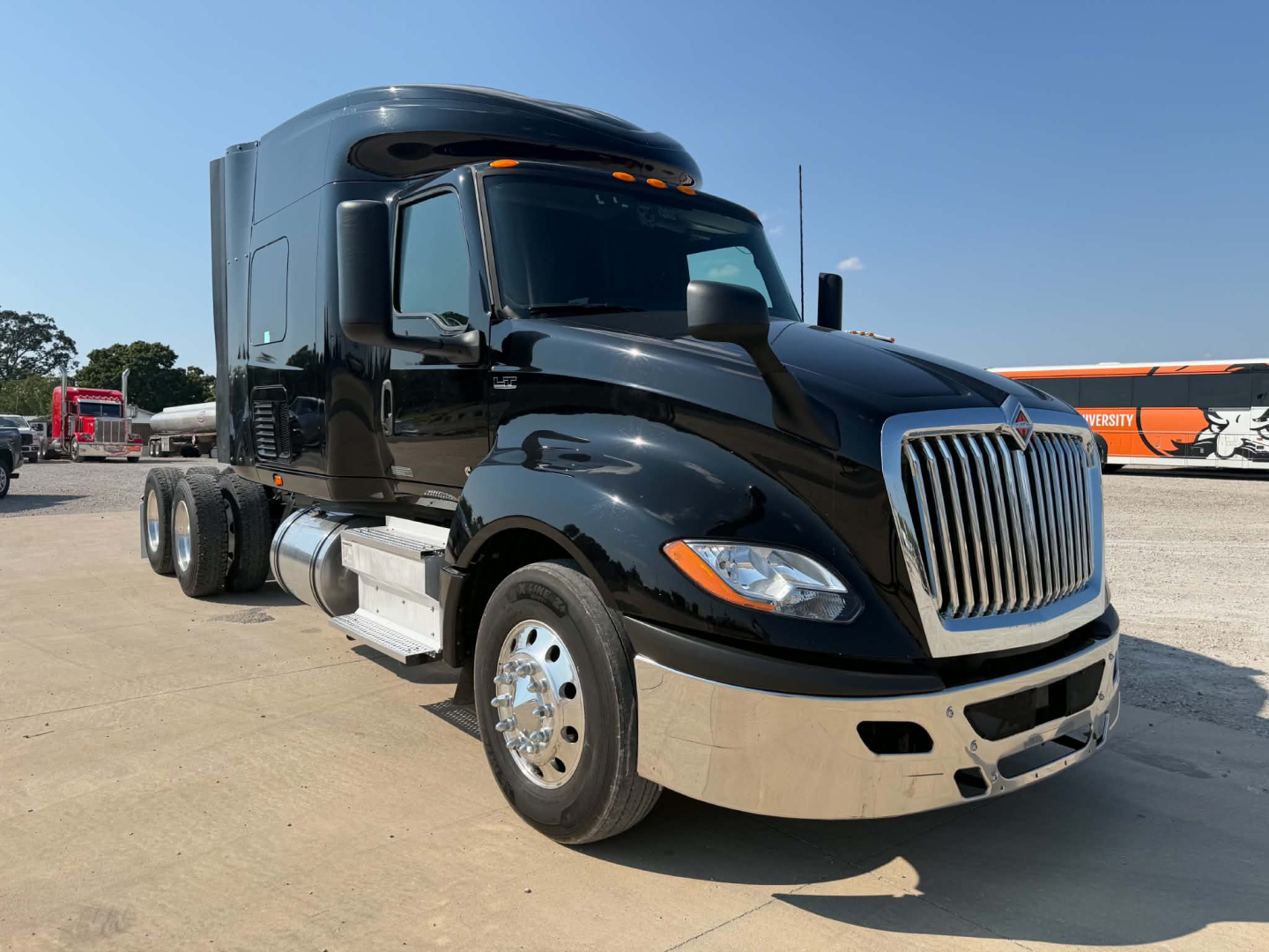 Truck cab front-left view showing chrome grille and black exterior. International LT625 tractor with sleeper, dual rear wheels, chrome bumper and fuel tanks.