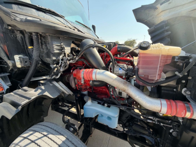 Engine bay of 2023 International LT625 showing red engine, large intake piping, coolant reservoir, and wiring harnesses.