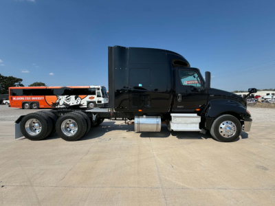 International LT625 truck side view showing sleeper cab and attached trailer with Oklahoma State University graphics.