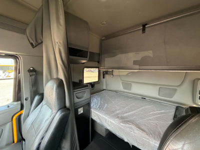 Interior of a 2023 International LT625 sleeper cab showing bunk bed with protective plastic, storage cabinets, and curtain divider.