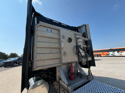 Image of a 2023 International LT625 dump truck with tipping bed raised, showing rear cab-mounted toolbox, fire extinguisher, and hydraulic lines.