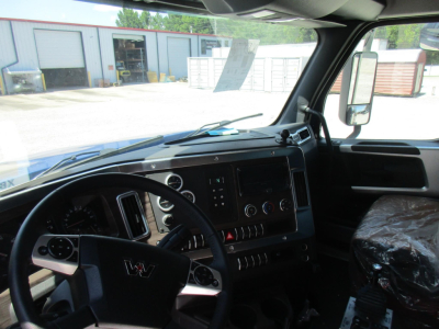 Interior of a 2027 Western Star 49X dump truck showing steering wheel, dashboard, control buttons, and driver seat with plastic cover.