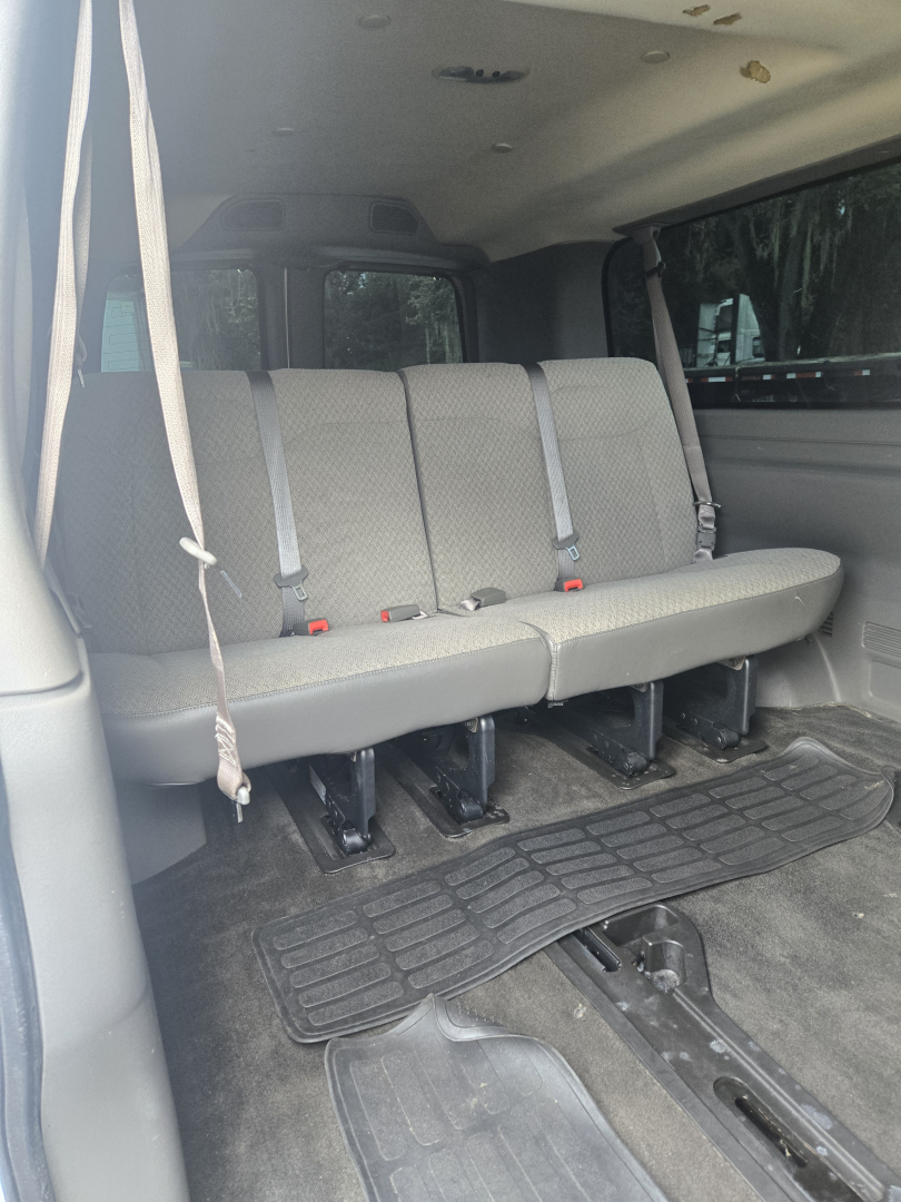 Chevrolet Express 3500 rear interior showing 3-row bench seat with grey upholstery and seatbelts, vinyl floor mats, and a cargo area.