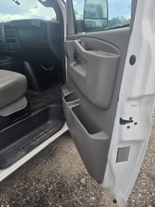Vehicle interior: front passenger door and open entry of a 2017 Chevrolet Express 3500 passenger van showing door panels, storage pockets, and dashboard area.