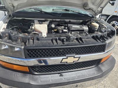 Chevrolet Express 3500 engine bay under hood; visible components include radiator, coolant reservoir, air intake, battery, and front grille with Chevrolet bowtie emblem.