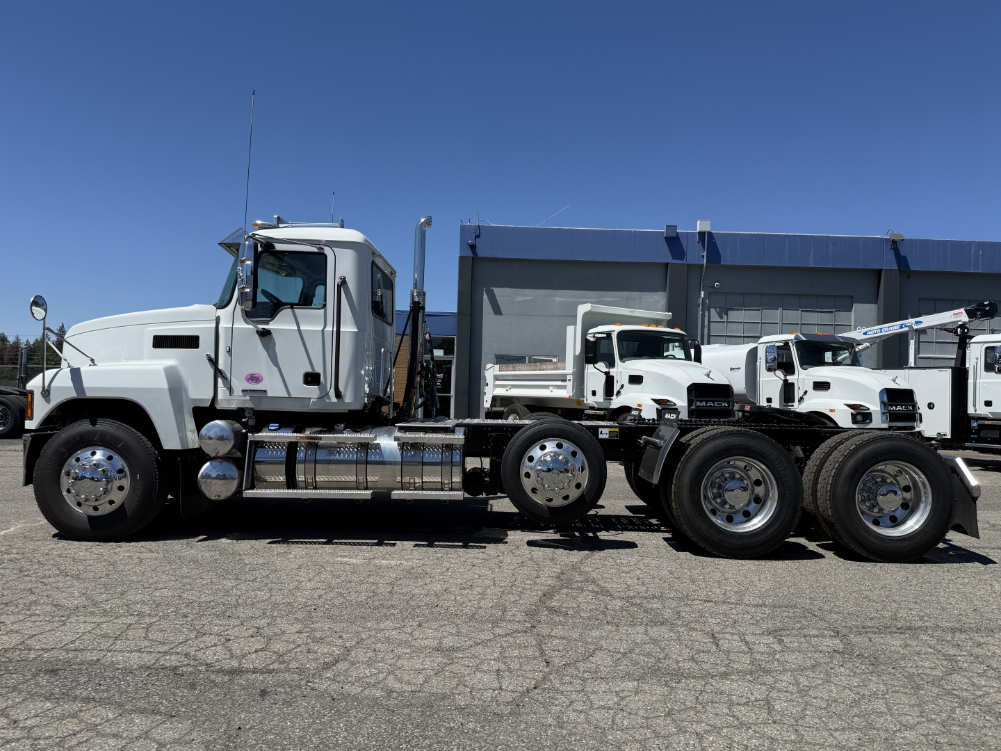 Side view of a white Mack PI84T conventional daycab truck with a tandem rear axle and chrome fuel tanks.