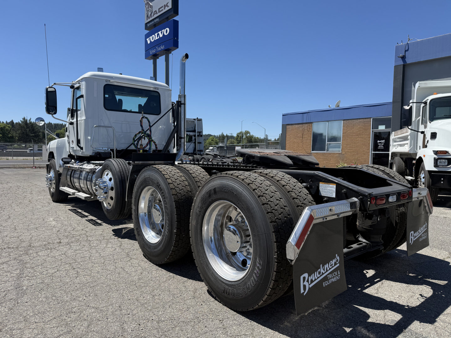 Mack PI84T conventional daycab truck chassis with dual rear axles and tires, cab front left, dealership lot in background