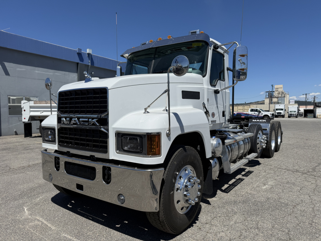Truck information label in front of a white Mack PI84T cab with chrome bumper and dual rear axles, showing 'MACK' grille and front headlights.