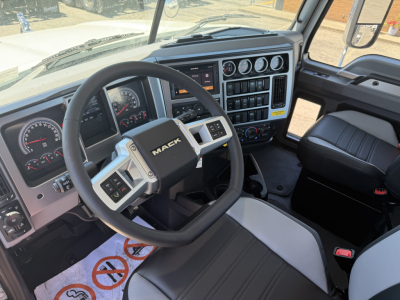 Dashboard and steering wheel of a Mack PI84T truck cab showing steering wheel with 'MACK' logo, gauge cluster, control panels, and center stack with vents and buttons.