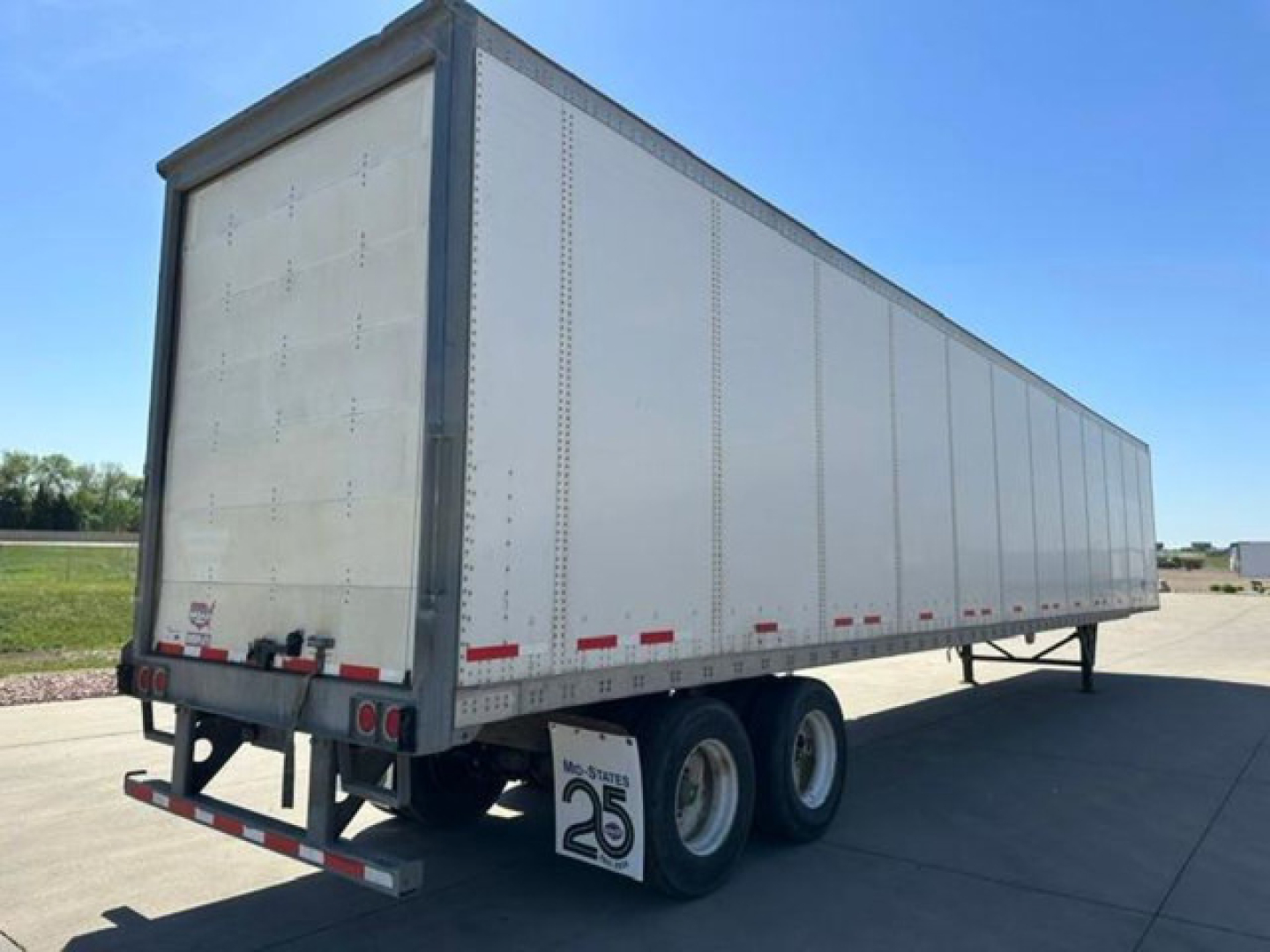 Trailer side view showing a 2016 Wabash trailer with dual rear wheels and reflective tape on the lower edge.
