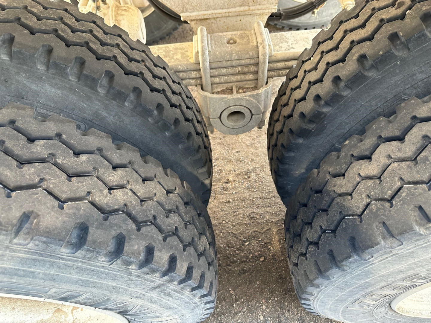 Dual rear tires of a dump trailer showing heavy tread pattern and suspension components between the tires.