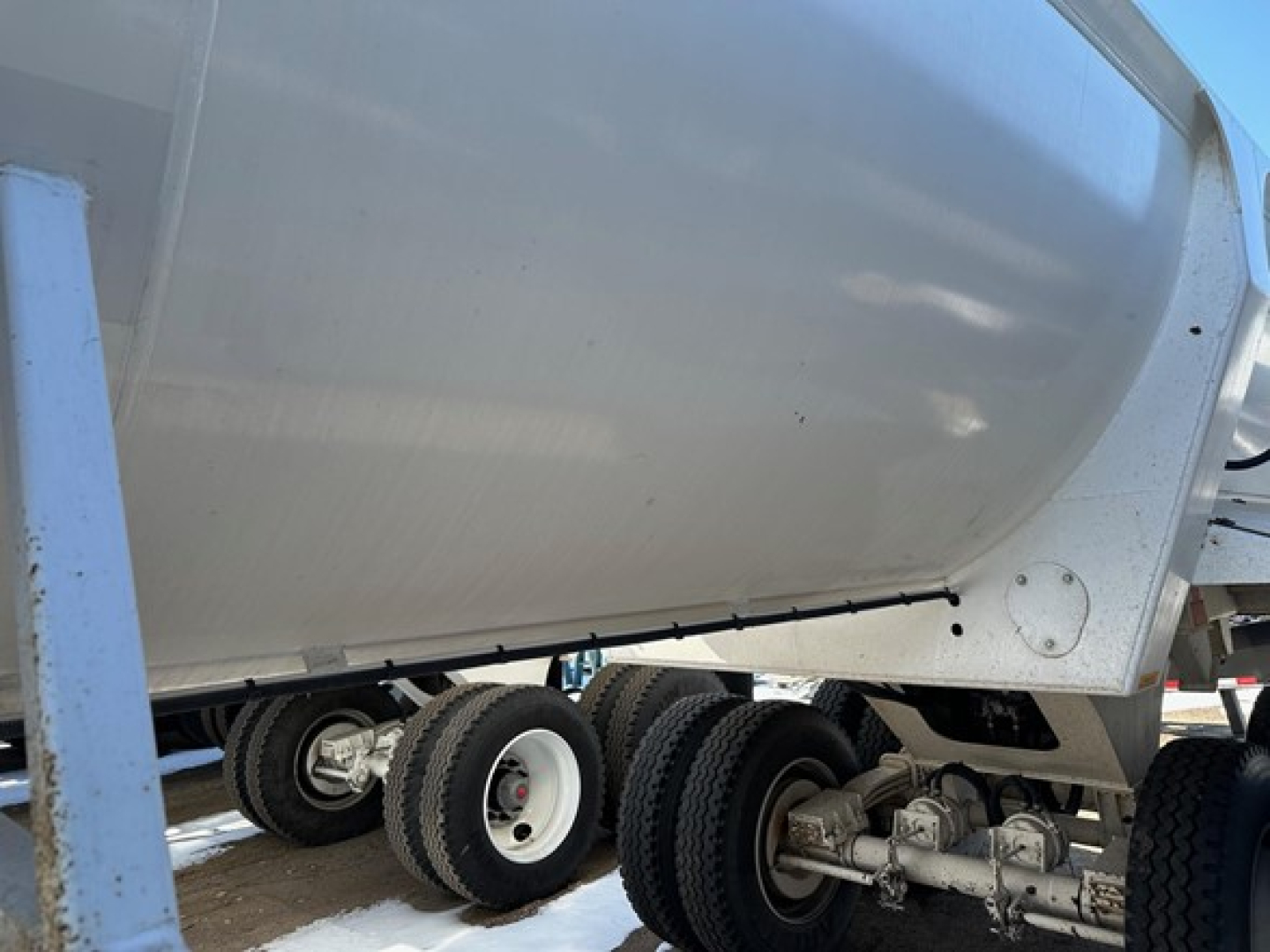 Dump trailer showing tandem axle wheel assemblies and side of aluminum dump bed with label plates.