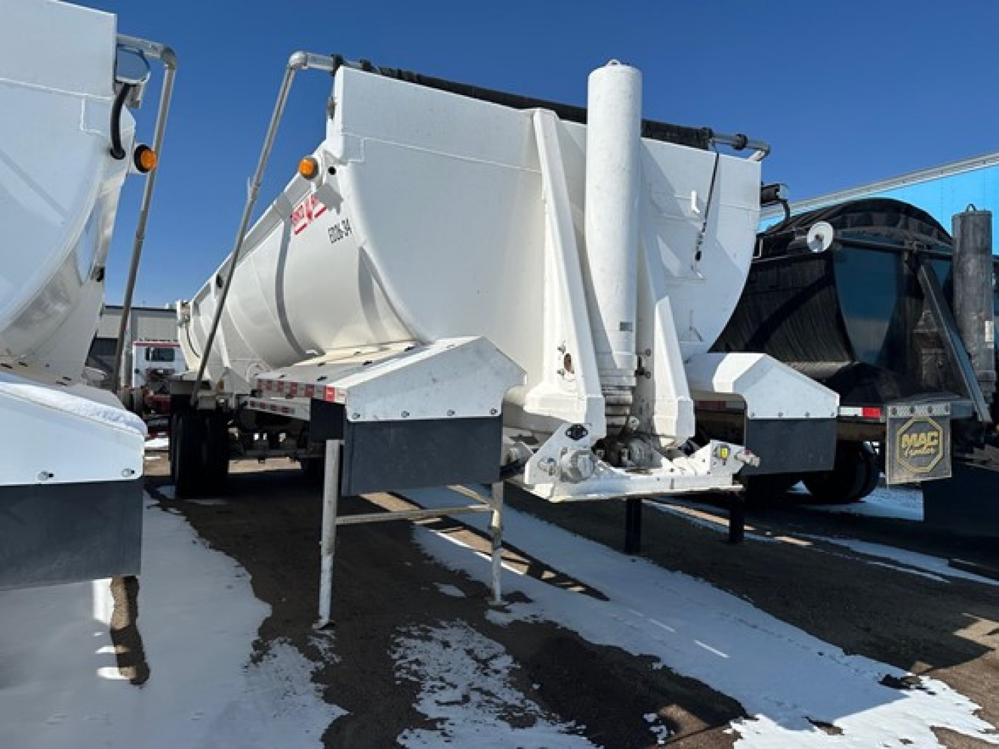 Dump trailer front view showing ED26-34-Ranco model with square nose, hitch, and support legs; white aluminum, side rails, and hydraulic compactor cylinder visible.