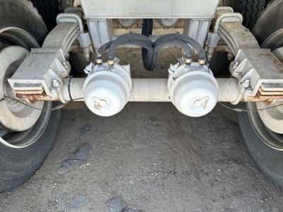 Dual air cylinders and hydraulic lines under a heavy trailer chassis showing coupling valves and hoses.