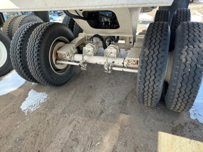 Trailer rear undercarriage showing dual-tandem axle with leaf springs and heavy-duty tires; multiple mechanical linkages and supports visible under the dump trailer.