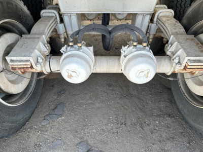 Dual air compressor housings and rear axle of a dump trailer showing two circular compressors with hoses connected, mounted under a metal frame between two wheels.
