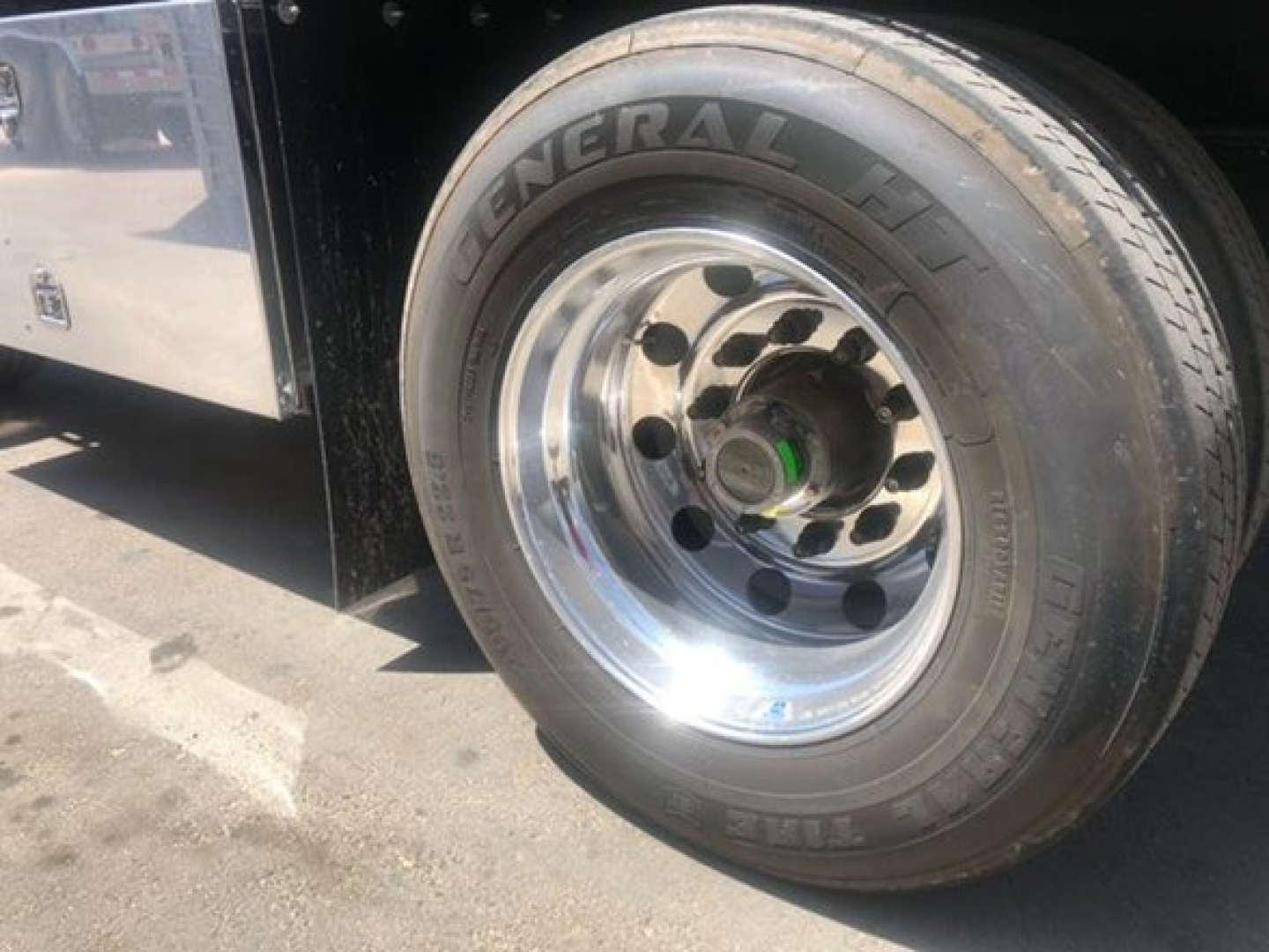 Trailer wheel area showing General HD tire on chrome wheel with green axle cap and black fender; part of flatbed trailer.