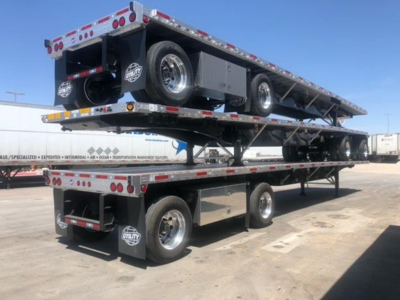 Flatbed trailer with dual level loading and spare tires stacked on top, chrome wheels, and reflective safety markings.