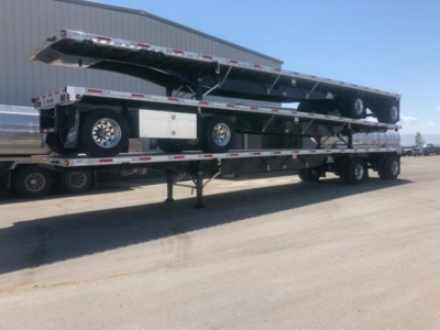 Flatbed trailer with a raised ramp on a multi-axle trailer, showing spare tire, storage box, and hydraulic components; a utility 4000Ae trailer in transport yard.
