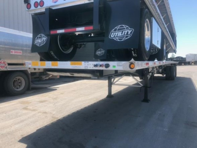 Utility trailer deck showing rear of flatbed with spare wheel, black mud flaps with Utility logo, and landing gear extended on a trailer.