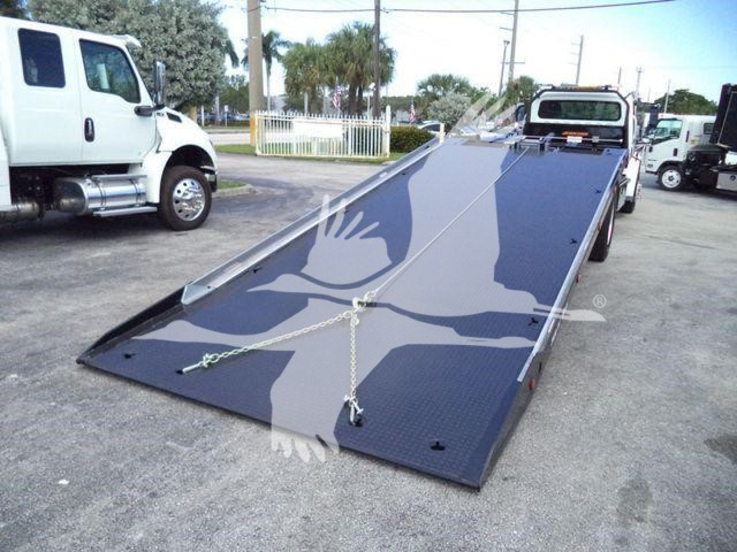 Freightliner M2 106 rollback truck with lowered flatbed ramp showing diamond plate surface and tiedown chains.