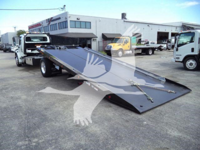 Flatbed tow truck with a lowered steel ramp in a dealership lot.