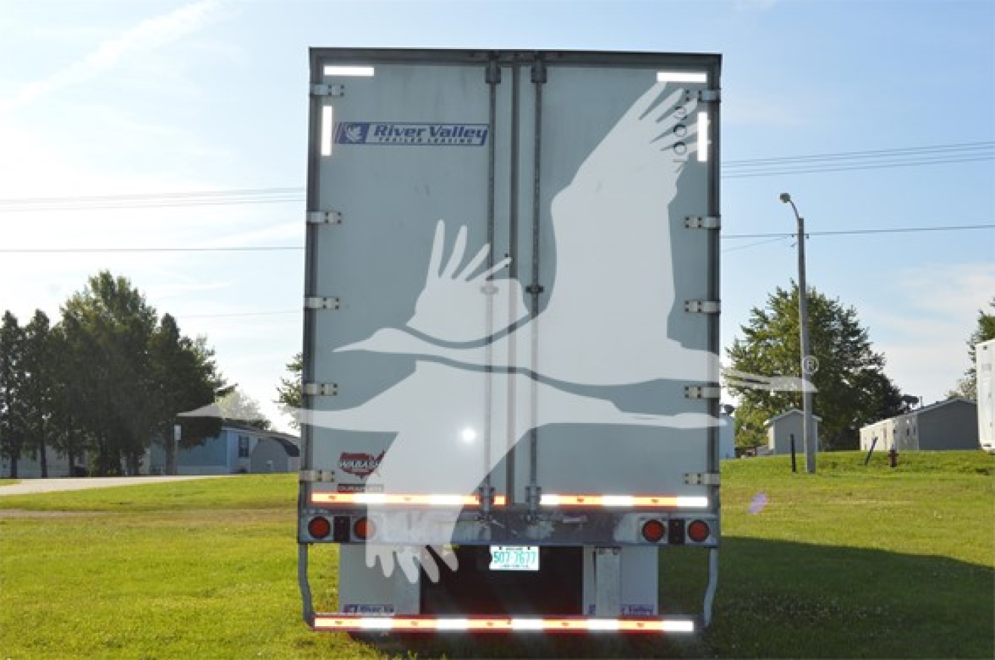 Rear view of a 2023 Wabash Duraplate trailer showing a large white graphic of birds in flight on the doors, River Valley logo, and rear lights.