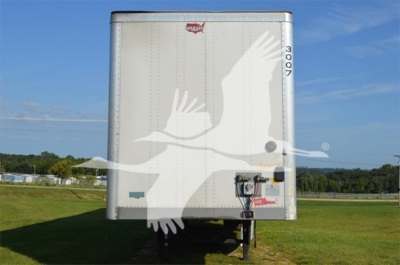 Front view of a silver Wabash trailer with logo and a white overlay of a bird. Visible text includes small manufacturer mark near top center and a vertical 'MOON' or 'MOON' sticker on right edge. Ground and blue sky in background.
