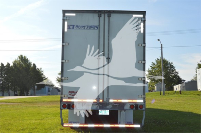 Rear view of a 2023 Wabash Duraplate trailer showing a large white graphic of birds in flight on the doors, River Valley logo, and rear lights.
