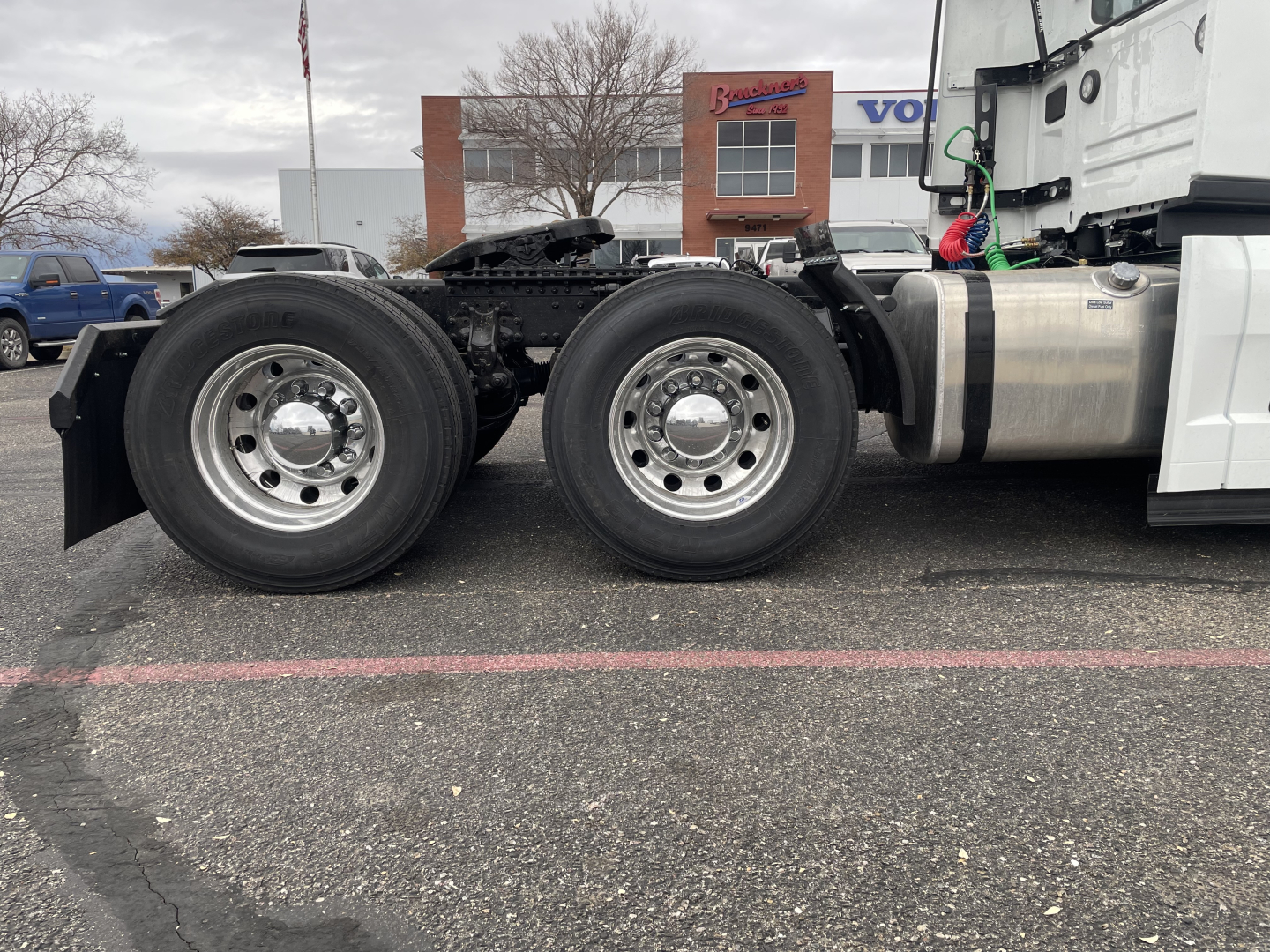 Conventional daycab truck rear three-quarter view showing dual rear axles with polished aluminum wheels and fuel tank, chassis and cab visible.