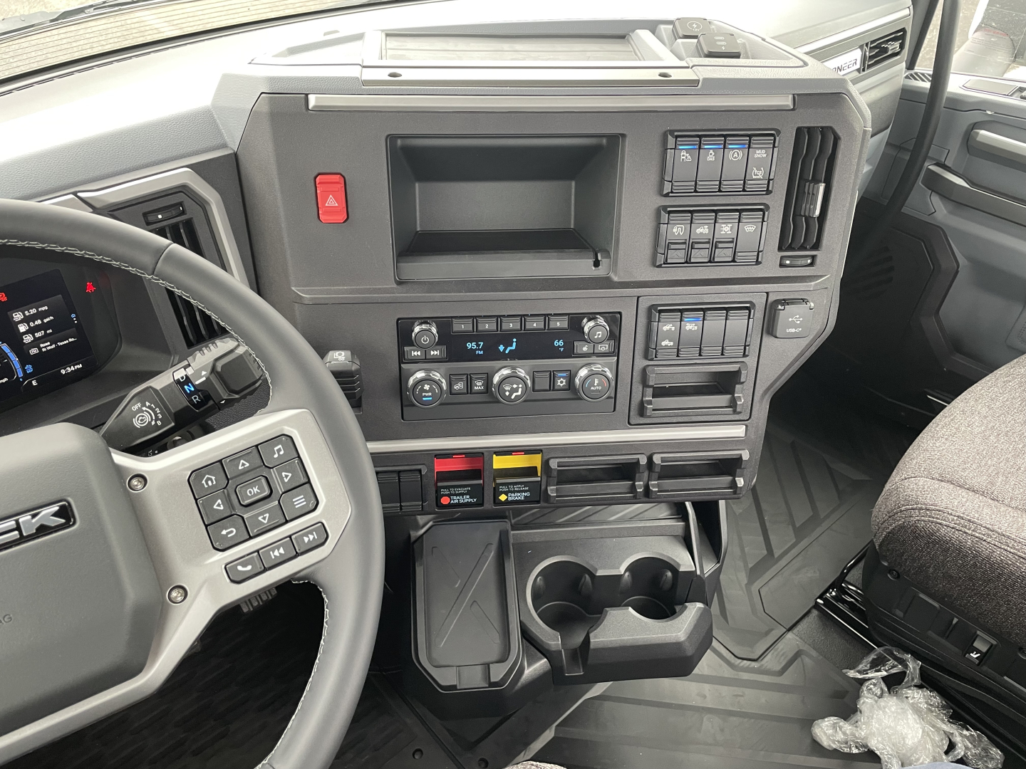Mack PR64T truck interior dash view showing steering wheel, control panels, gear shifter, and center console with cup holders.