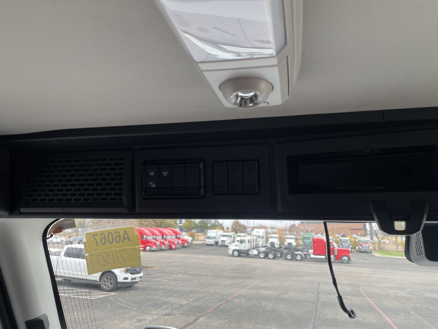 Interior view of Mack PR64T cab area with overhead controls and sun visor, windshield view showing yard with trucks.