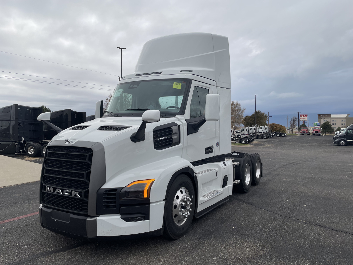 Mack PR64T clean white tractor with sleeper cab, front grille, large wheels, and elevated exhaust, side mirrors, and hood air intake in a dealership lot.