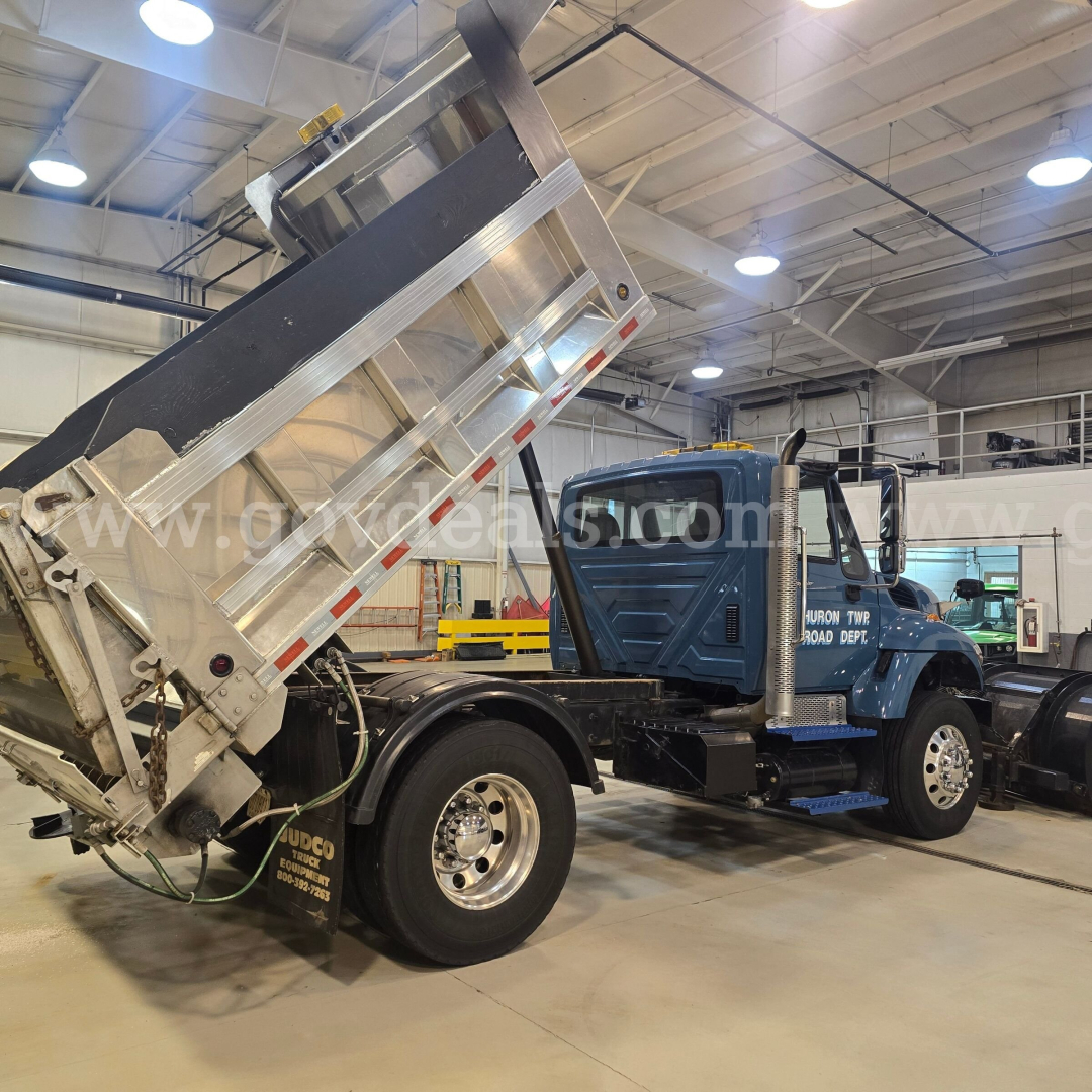 Truck cab and hydraulic dump bed on a plow truck in a shop. Side shows International logo and dump bed raised.