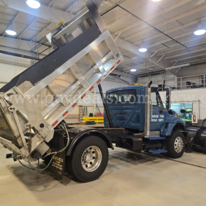 Truck cab and hydraulic dump bed on a plow truck in a shop. Side shows International logo and dump bed raised.