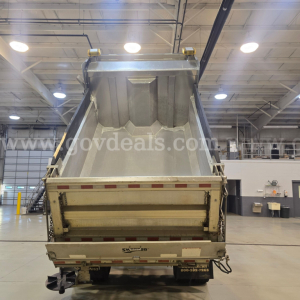 Dump truck bed with rear tailgate and plow equipment in a showroom, International 7400 model, tail lights and reflective tape visible.