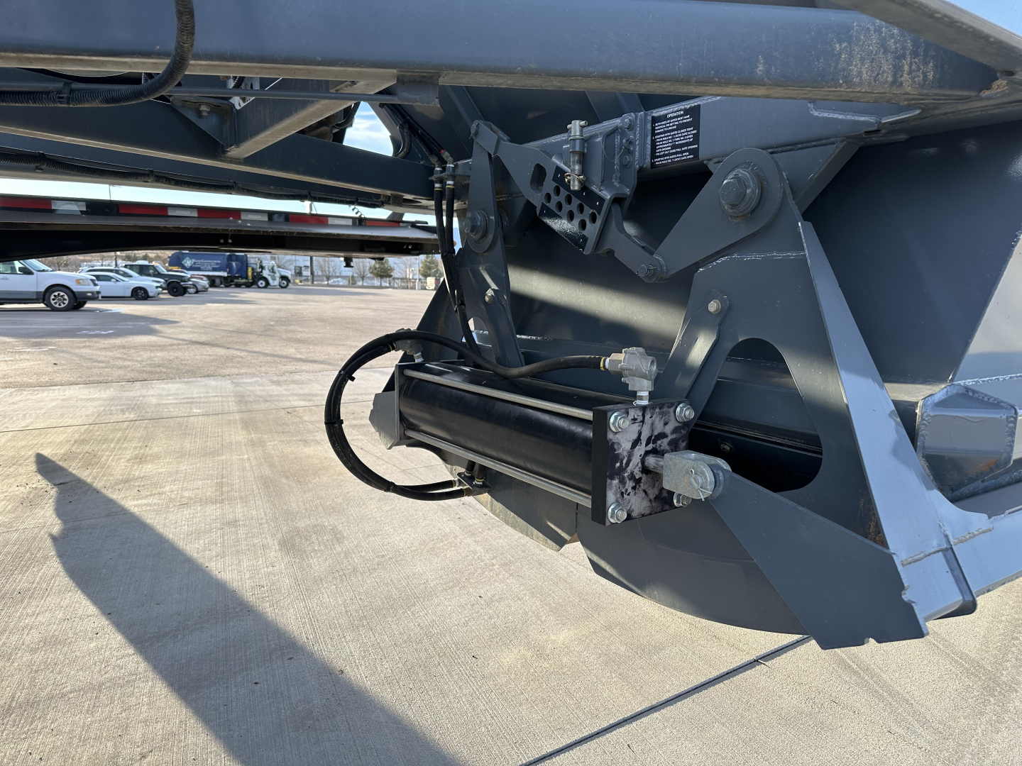 Dump trailer hitch area showing hydraulic cylinder and linkage, with metal frame and support components visible.